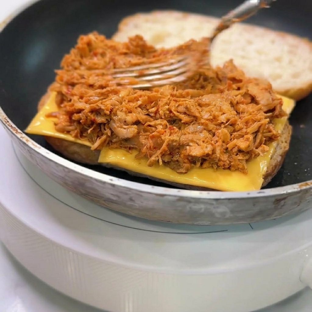 Eine Gabel verteilt eine dicke Schicht des Hähnchens in Sauce auf dem Käse im Ciabatta.