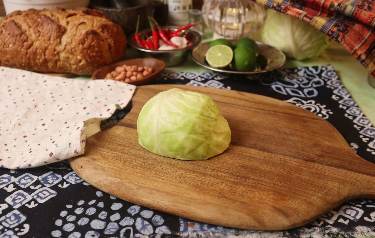 Ein Viertel Weißkohl auf einem Holzbrett neben einem rustikal gemusterten Tuch.