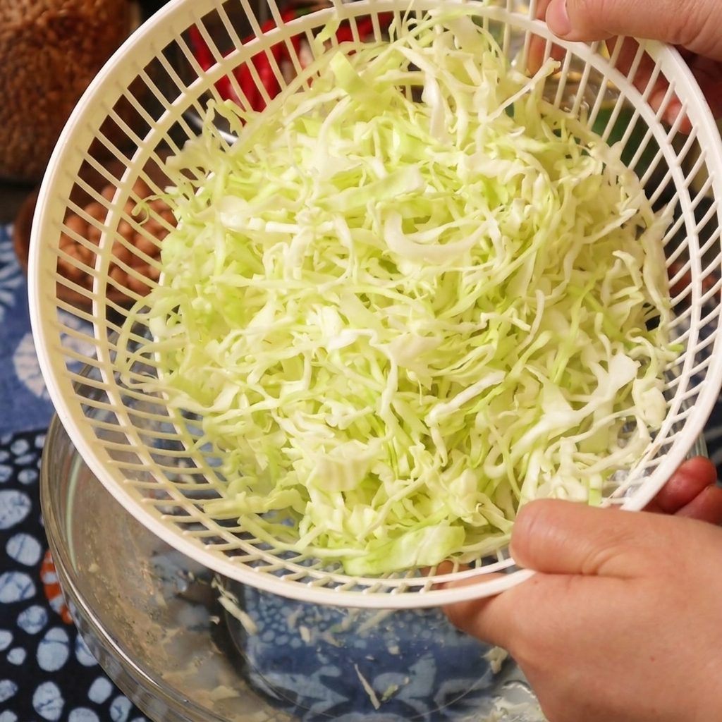 Eine Person hält eine weiße Salatschleuder mit frisch getrocknetem, geschnittenem Kohl.