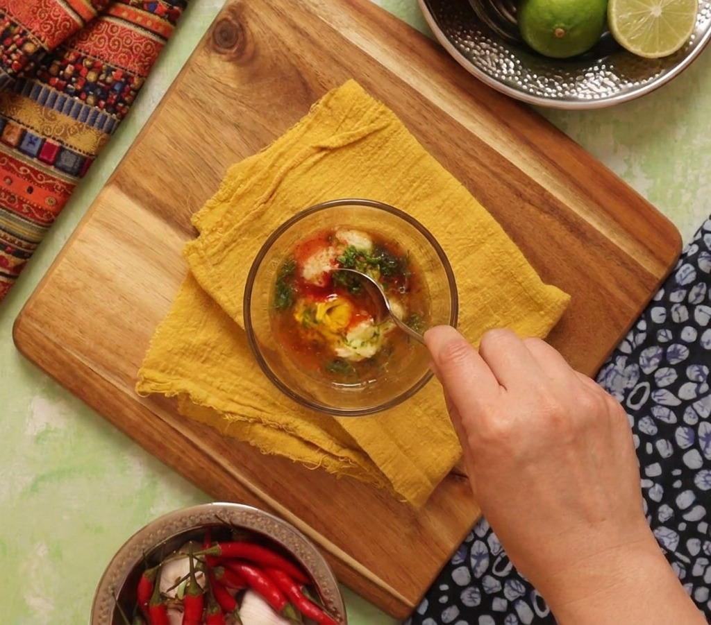 Eine Hand rührt eine orangefarbene Sauce aus Mayo, Limette und Gewürzen mit einem Metalllöffel um.