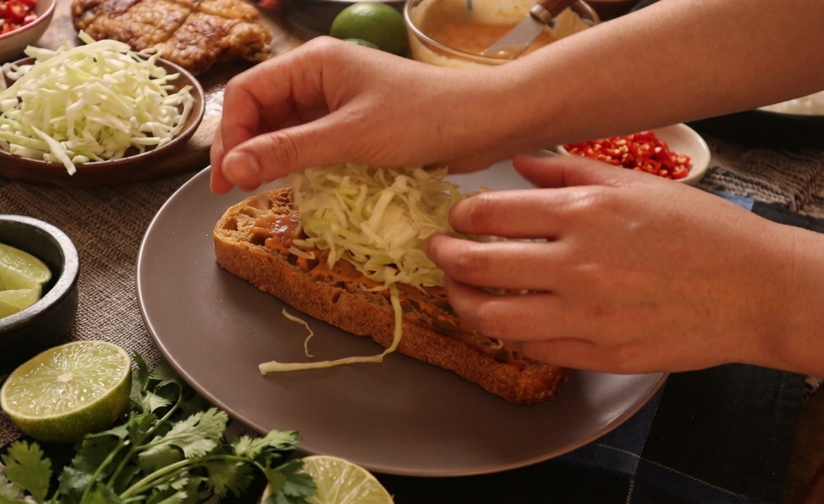 Hände platzieren einen hohen Haufen fein geschnittenen Weißkohl auf eine mit Sauce bestrichene Scheibe Brot.