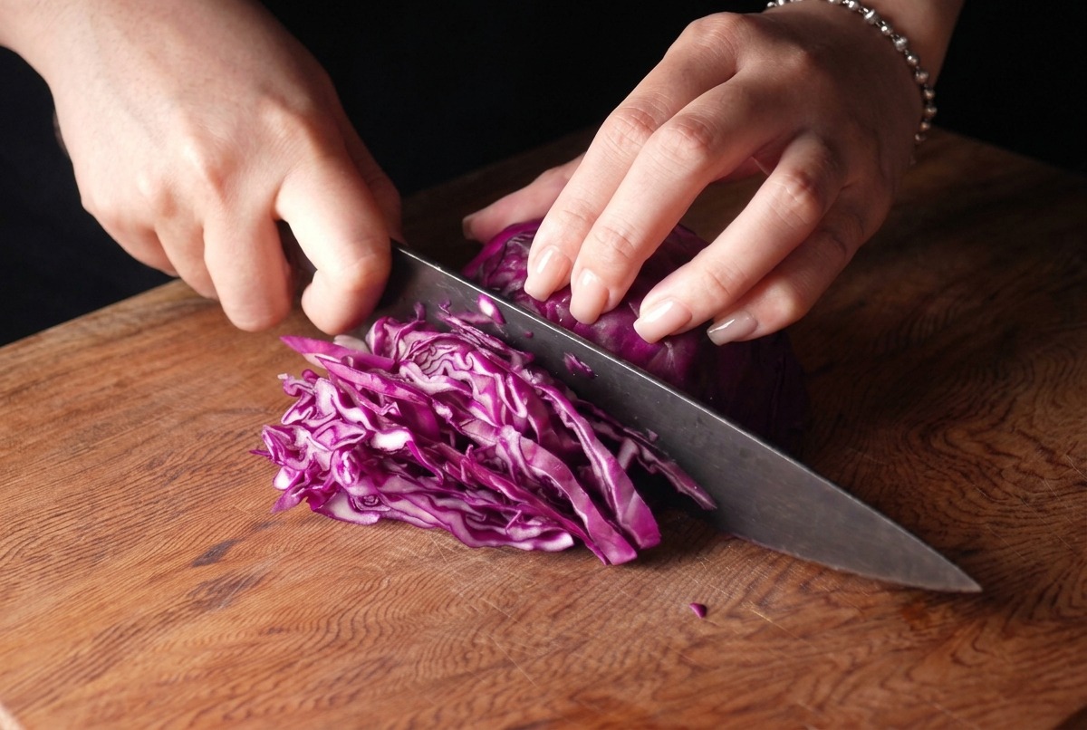 Eine Person schneidet einen Rotkohl mit einem Kochmesser in feine Streifen.