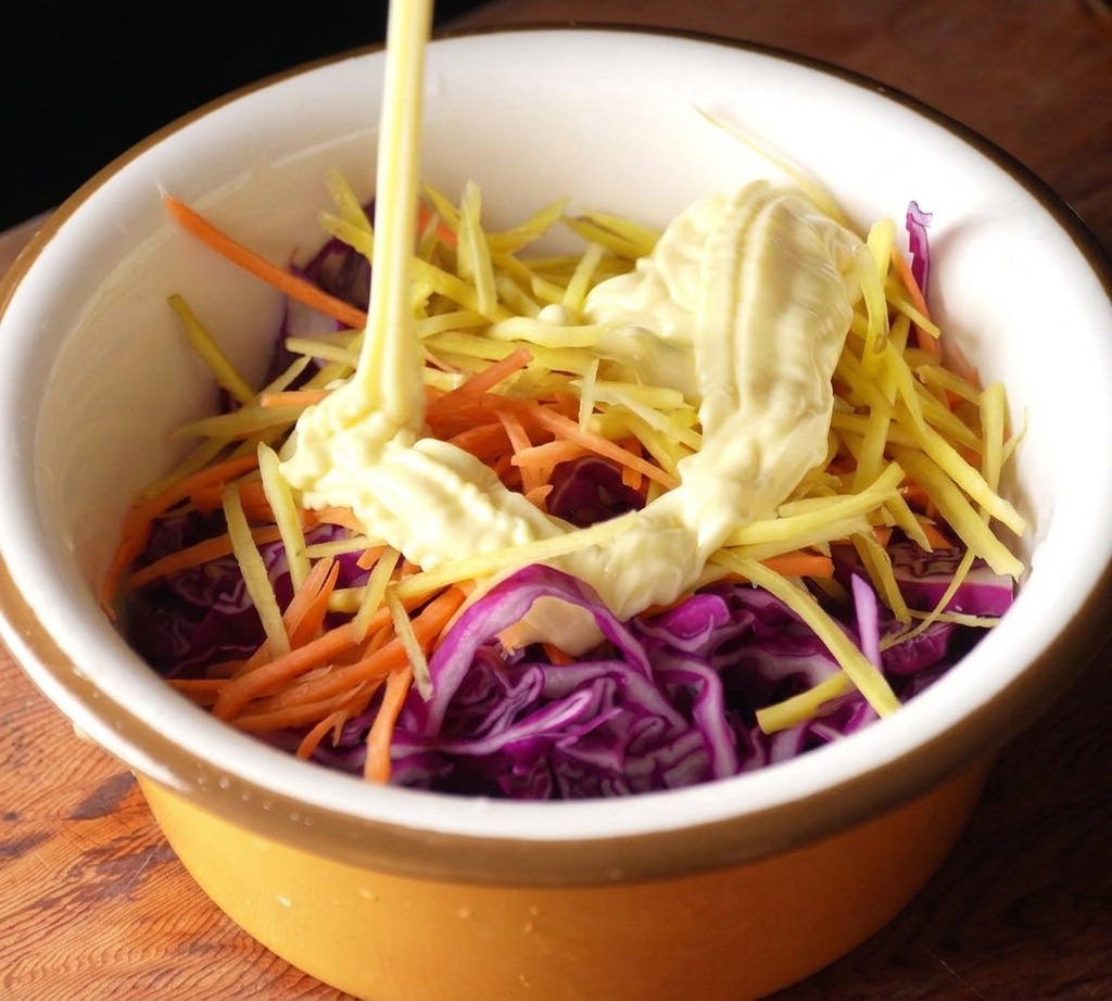 Mayonnaise wird aus einer Flasche in eine Schüssel mit Rotkohl und Karotten gegeben.