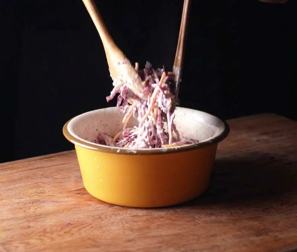 Rotkohl und Karotten werden mit Holzwerkzeugen in einer gelben Schüssel vermengt.