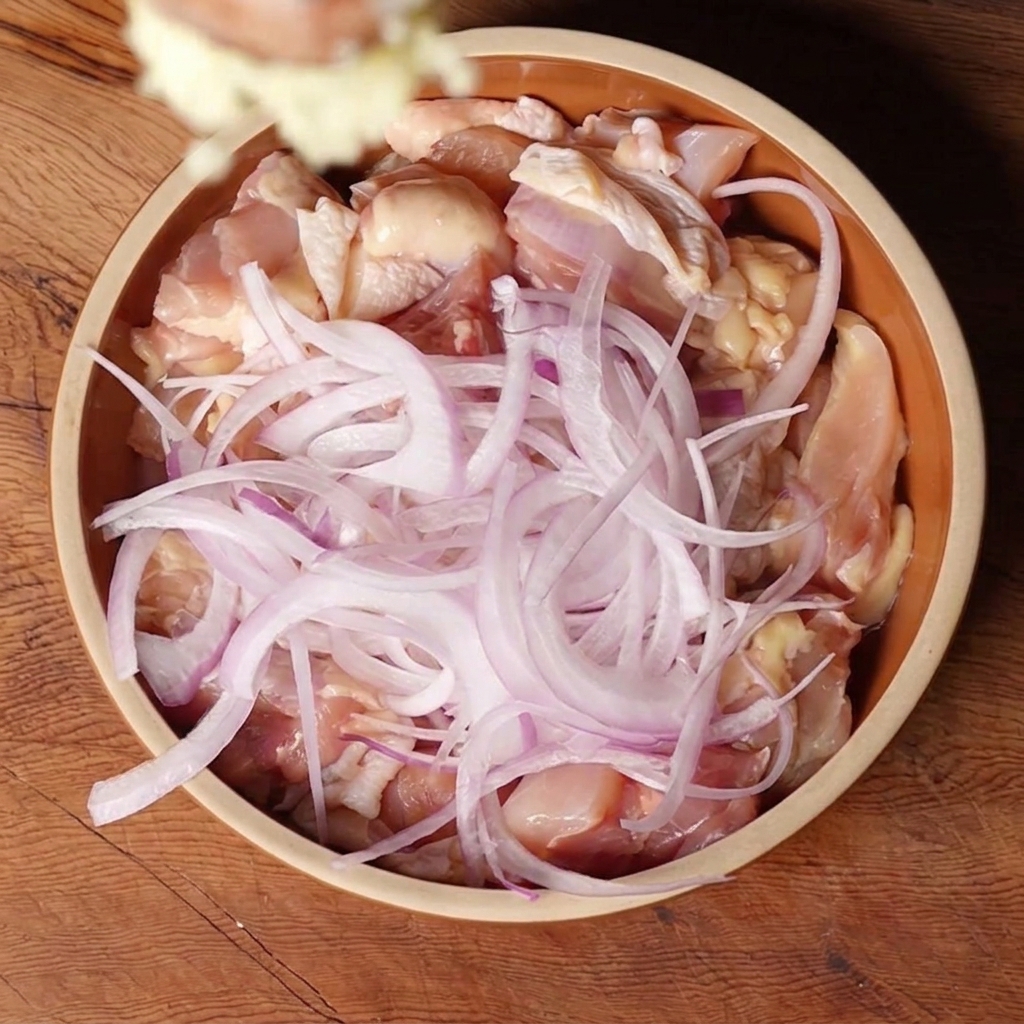 Gehackter Knoblauch und Ingwer werden in eine Schüssel mit Hähnchen und Zwiebeln gegeben.