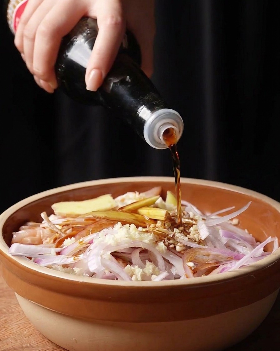 Sojasauce und Fischsauce werden über das rohe Hähnchen und die Aromaten gegossen.
