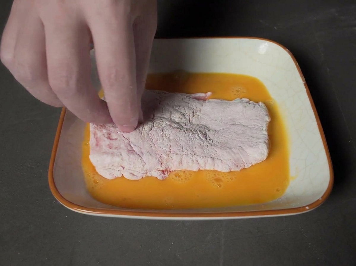 Eine Hand drückt das in Ei getauchte Schnitzel fest in eine Schale mit Panko-Brotkrumen.