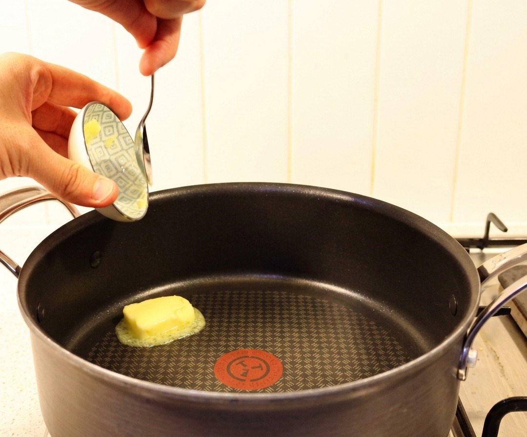 Ein Stück gelbe Butter wird mit einem Löffel in eine heiße schwarze Pfanne gegeben.