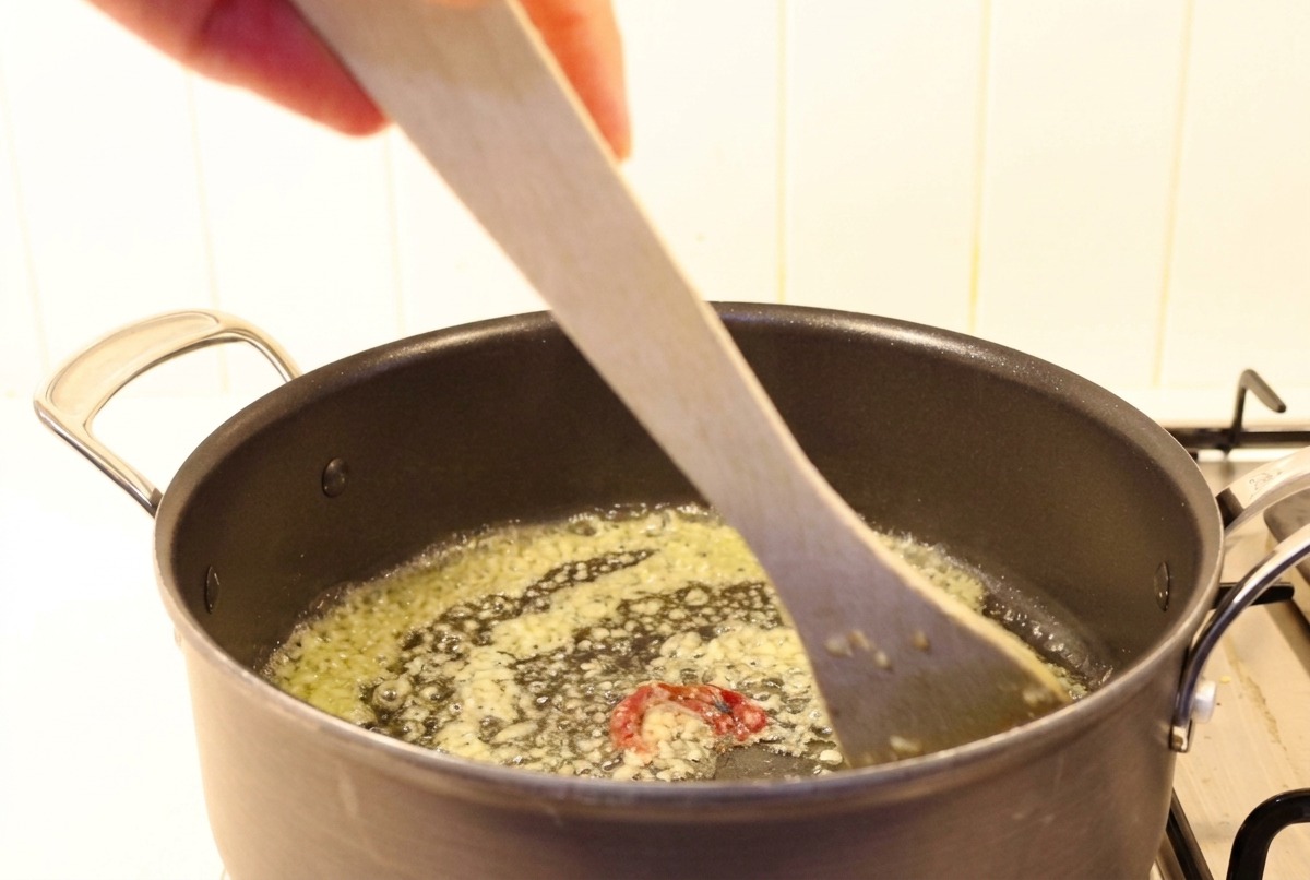 Gehackter Knoblauch und Chili werden in geschmolzener Butter mit einem Holzspatel umgerührt.