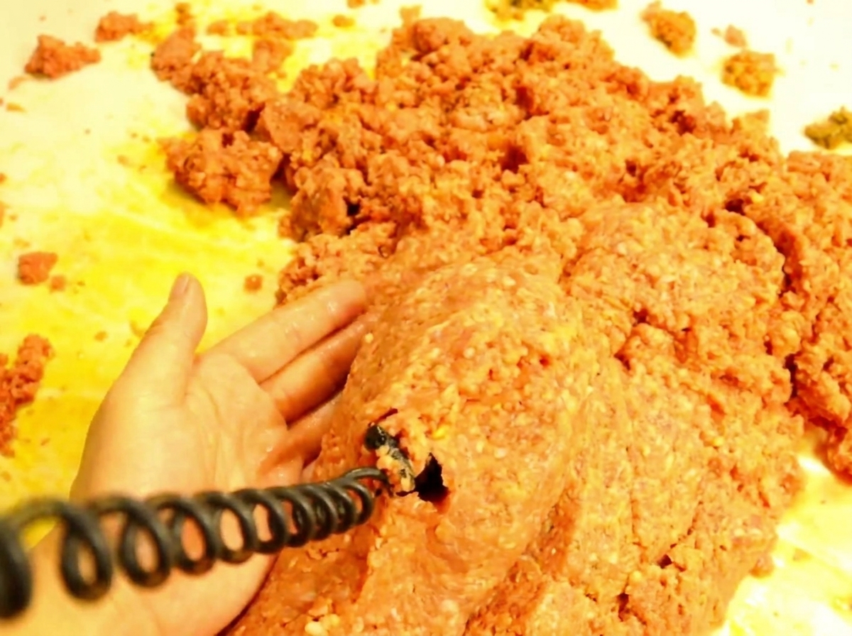 Ein Holzlöffel gibt eine Portion der heißen Fleischsauce auf ein geröstetes Hamburger-Brötchen.