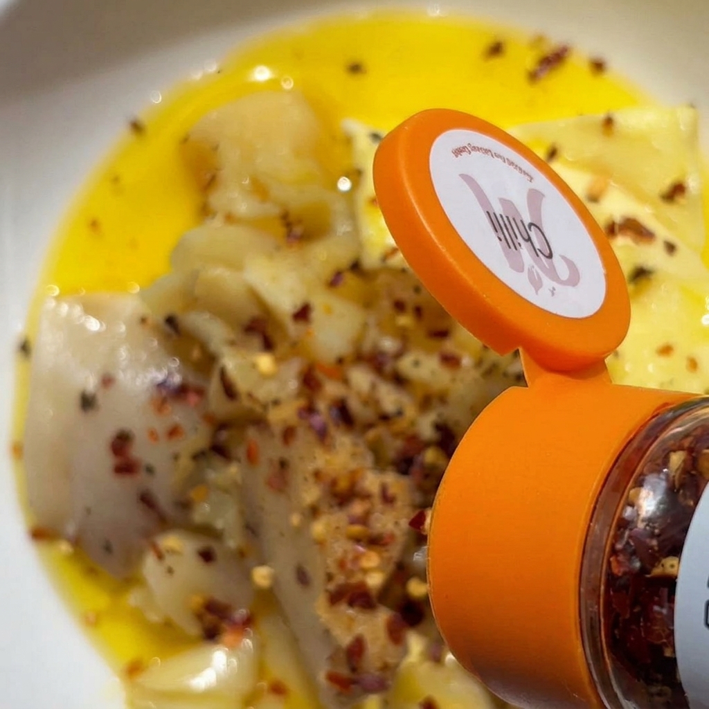 Chiliflocken werden aus einem Gewürzstreuer über eine Schüssel mit zerdrücktem Knoblauch und Butter gestreut.