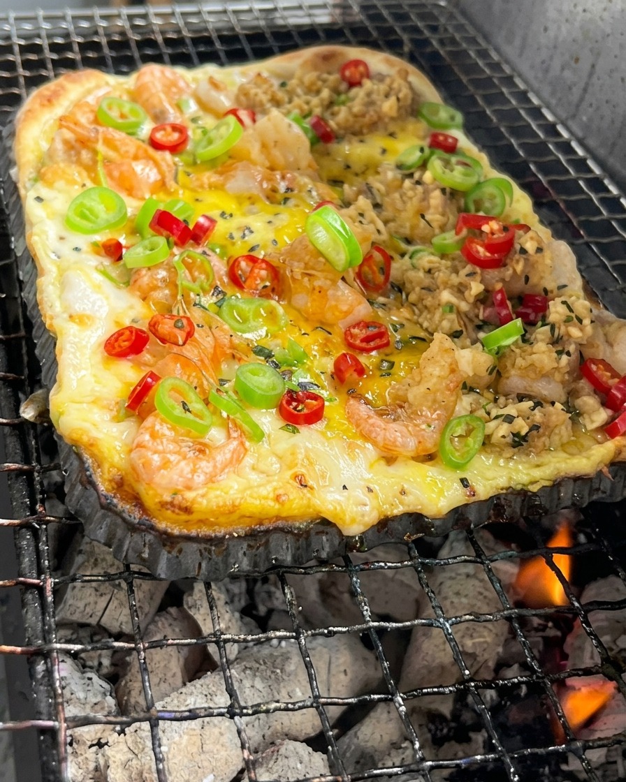Ein rechteckiger Pizzateig mit Garnelen und Gemüse backt über glühender Holzkohle.