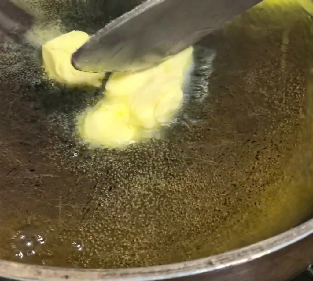 Gelbe Butterwürfel schmelzen und blubbern in einer dunklen Pfanne bei schwacher Hitze.