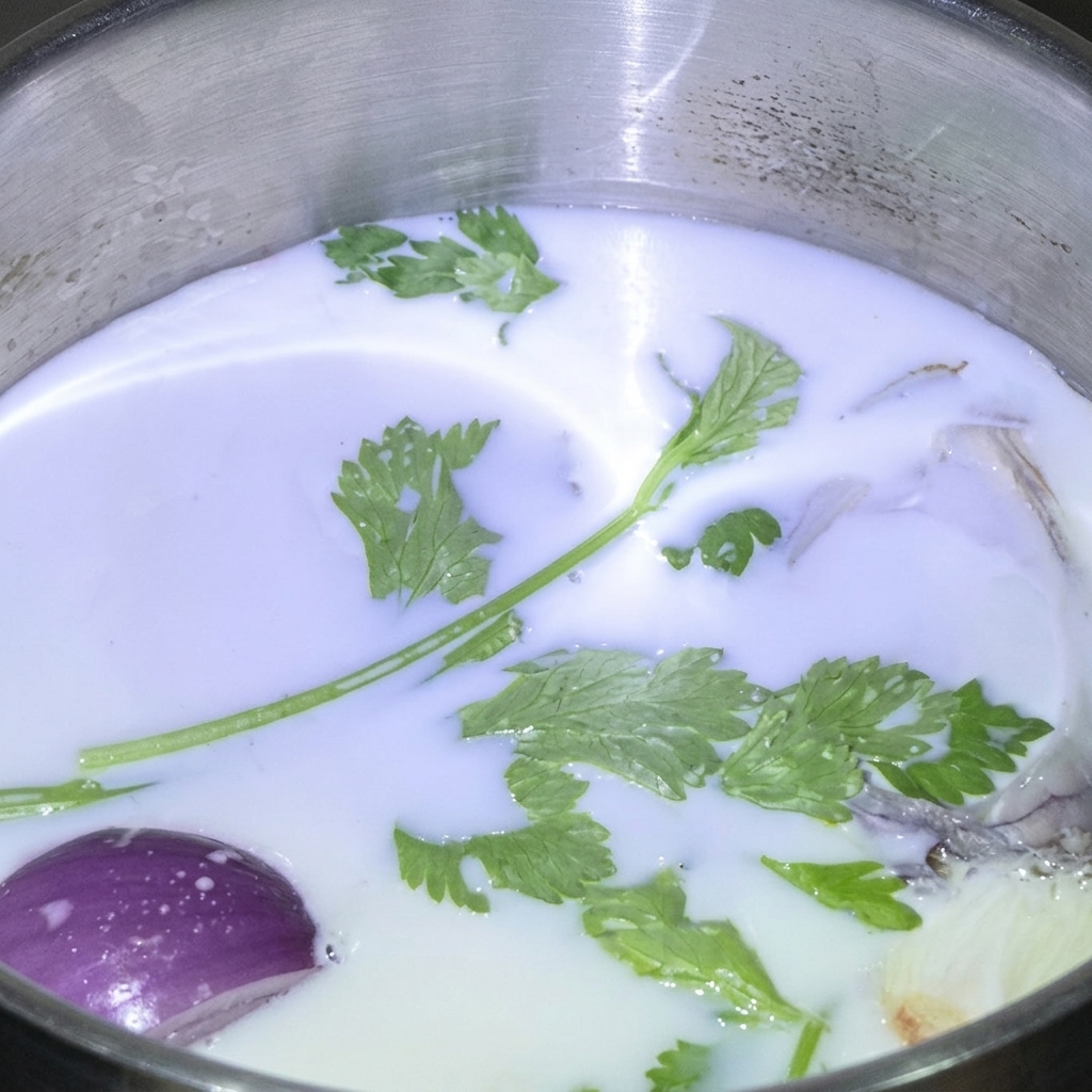 Frische grüne Kräuter und ein Stück rote Zwiebel schwimmen in einem Edelstahltopf mit weißer Milch.