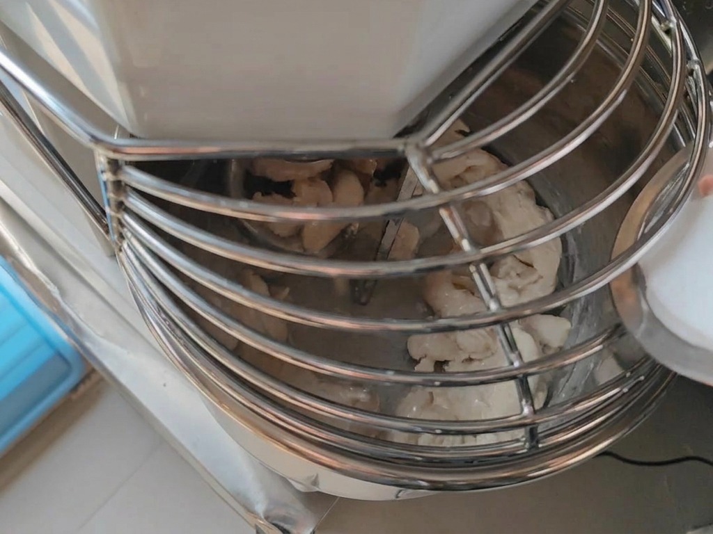 Aus einem kleinen Behälter wird feines Salz in eine Spiral-Knetmaschine gegossen, während der Pizzateig geknetet wird.
