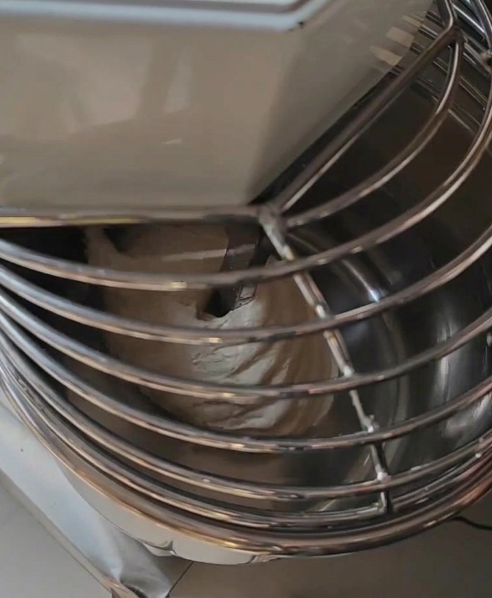 Eine professionelle Spiral-Knetmaschine enthält eine große Portion glatten Pizzateig unter einem Metall-Schutzgitter.
