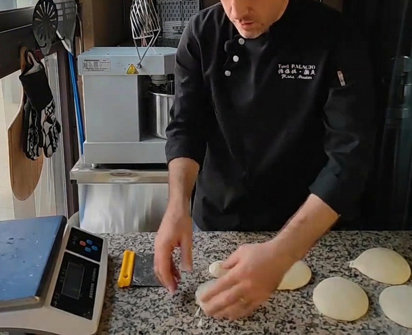 Mehrere glatte, runde Pizzateigkugeln liegen nach dem Formen von Hand auf einer Granitarbeitsplatte.