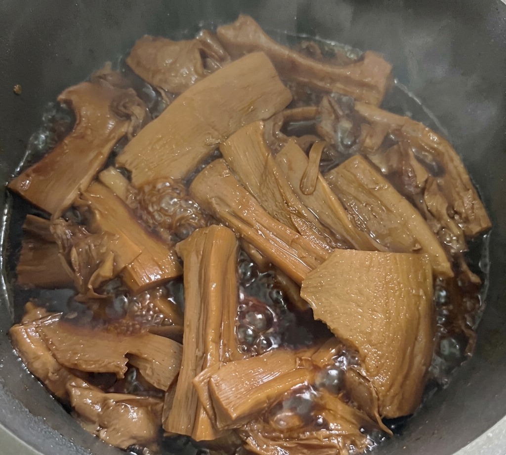 In Scheiben geschnittene Bambussprossen köcheln in einer blubbernden, dunkelbraunen Würzsauce in einem Metalltopf auf dem Herd.