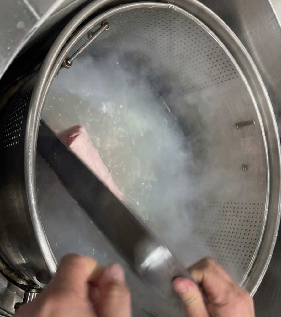 Saubere, helle Schweinefüße werden in einem Metallgitterkorb in einen großen Topf mit klarem, kochendem Wasser gelassen.