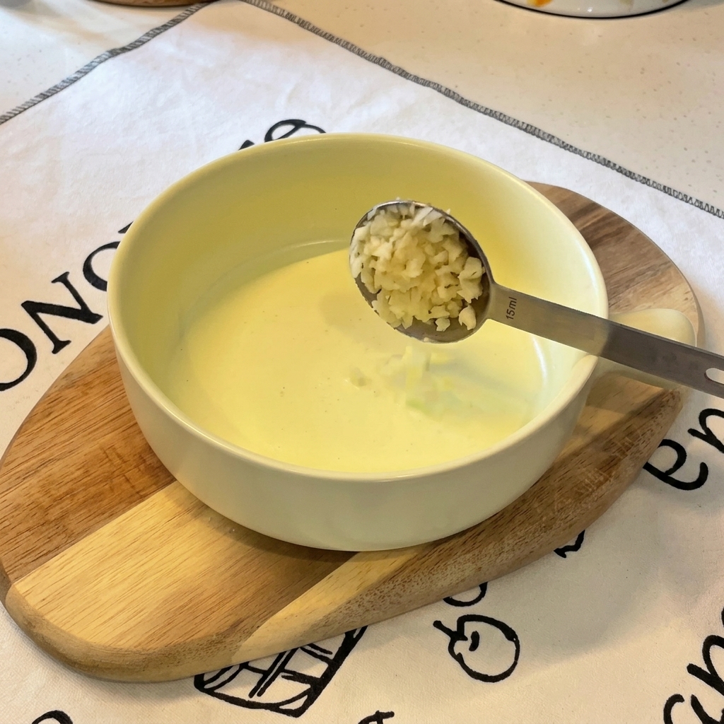 Ein Messlöffel aus Metall gibt fein gehackten Knoblauch in eine Schüssel, in der sich bereits einige gehackte Frühlingszwiebeln befinden.
