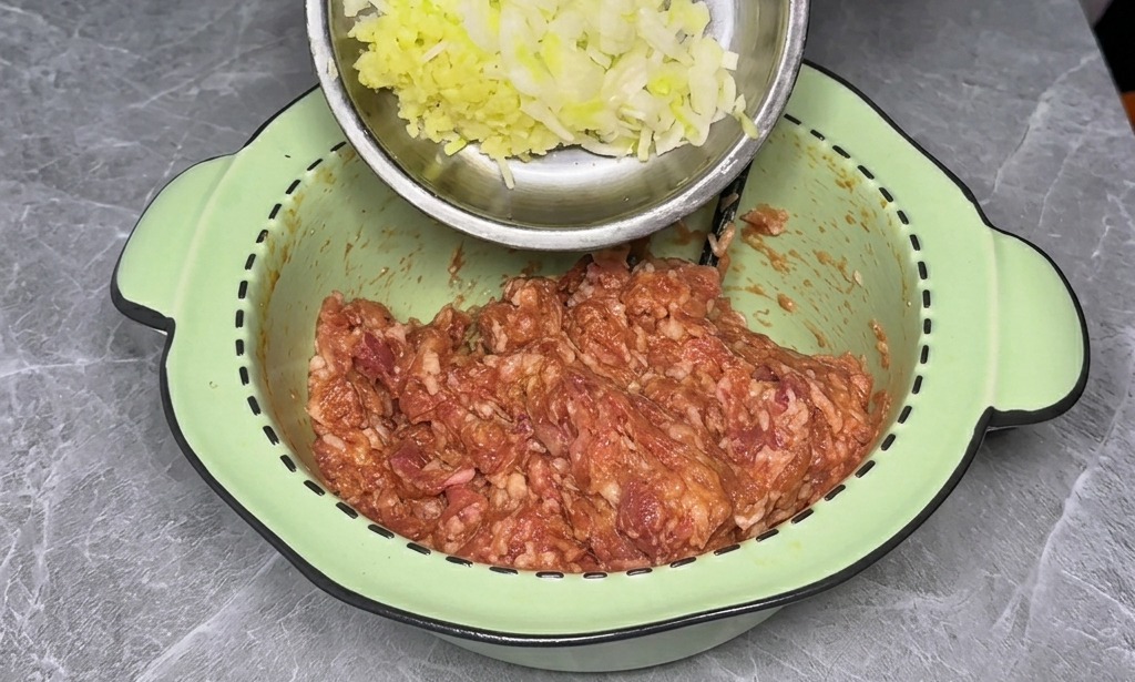 Eine Hand hält eine kleine Edelstahlschale mit gehackten Frühlingszwiebeln und Ingwer über eine Schüssel mit gewürztem Fleisch.