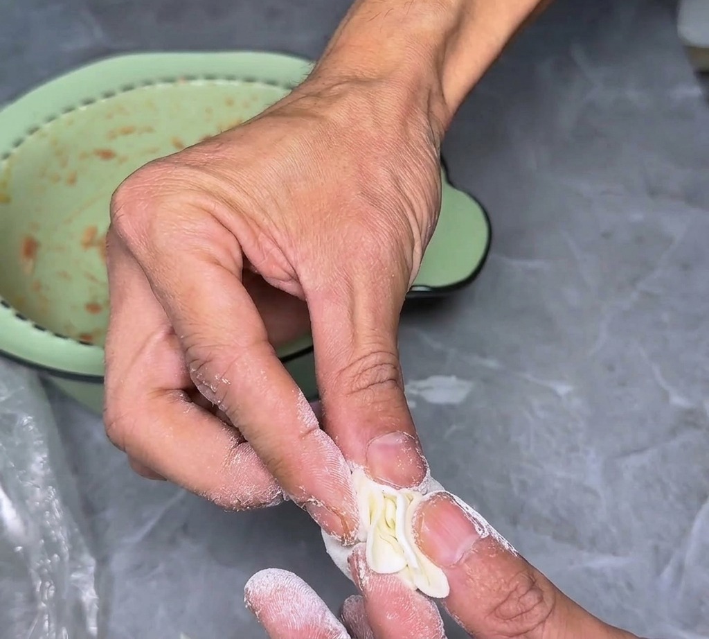 Nahaufnahme von Fingern, die die gefalteten Ränder eines Wantan-Teigblatts zusammendrücken, um einen dekorativen und funktionellen Verschluss zu schaffen.