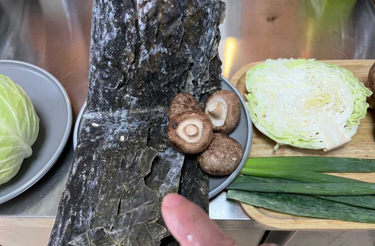 Verschiedene frische Zutaten wie Kohl, Kombu-Seetang und Shiitake-Pilze auf einer Küchenzeile bereitgestellt.