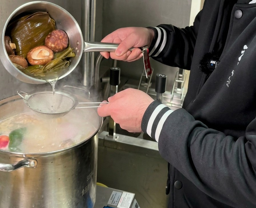 Eine goldfarbene Pilz- und Kombu-Flüssigkeit wird durch ein Sieb in einen großen Topf mit kochender Brühe gegossen.