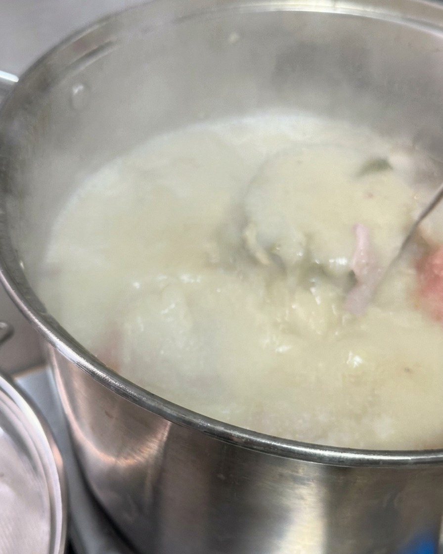 Milchig-weiße Schweinebrühe wird durch ein Metallsieb in einen Topf gegossen, der eine dunkle Sauce und Schmalz enthält.