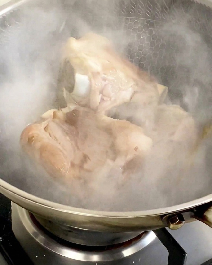 Dichter weißer Dampf steigt aus dem Wok auf, nachdem Kochwein zu den angebratenen Knochen gegeben wurde.