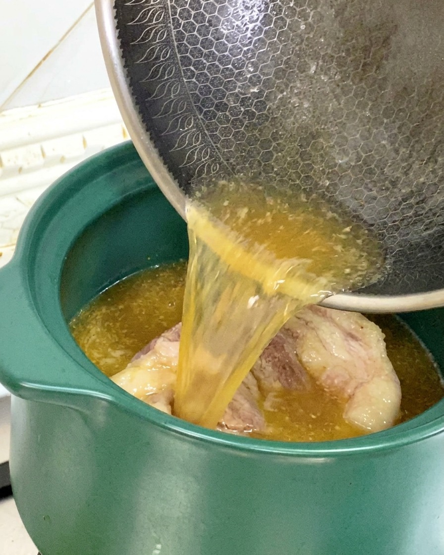 Die angebratenen Schweineknochen samt Bratensaft werden aus der Pfanne in einen grünen Tontopf gegossen.