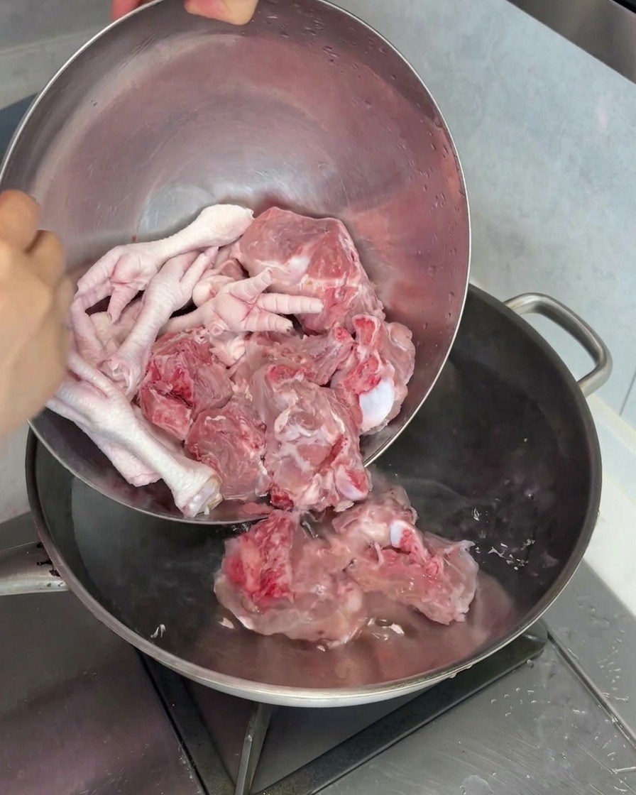 Rohe Schweinsmarkknochen und Hühnerfüße werden zum Blanchieren in einen Topf mit Wasser gegeben.