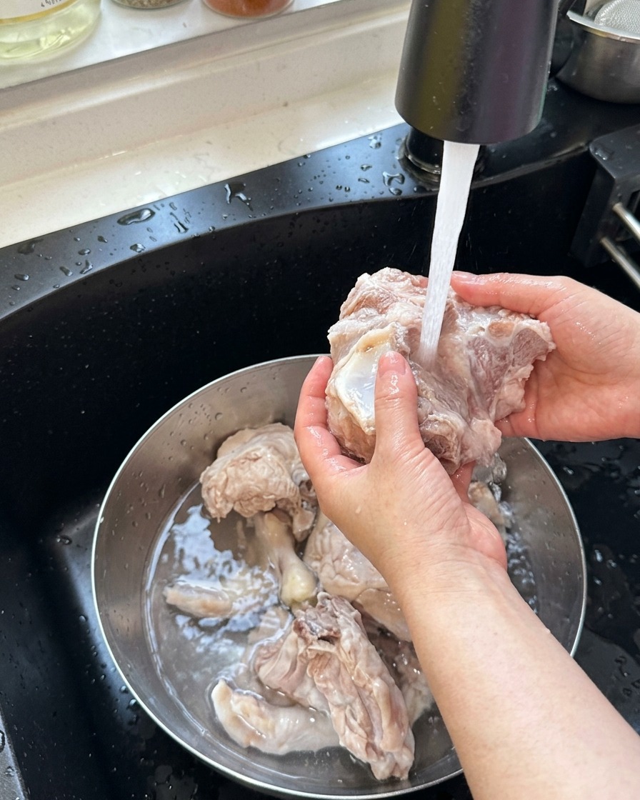 Blanchierte Schweineknochen und Hühnerfüße werden unter warmem, fließendem Wasser abgespült.