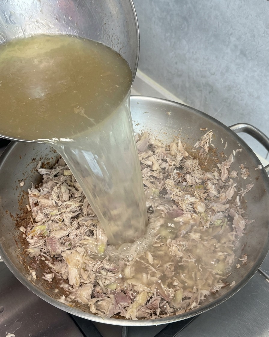 Eine Kelle gießt klare, goldene Brühe in einen Wok mit angebratenen Fleischresten, wodurch bei Kontakt eine trübe, weiße Reaktion entsteht.