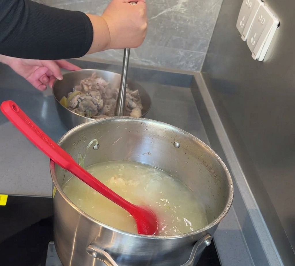 Eine Hand benutzt einen Kartoffelstampfer aus Metall, um gekochtes Schweinefleisch und Mark in einer Schüssel zu zerdrücken.