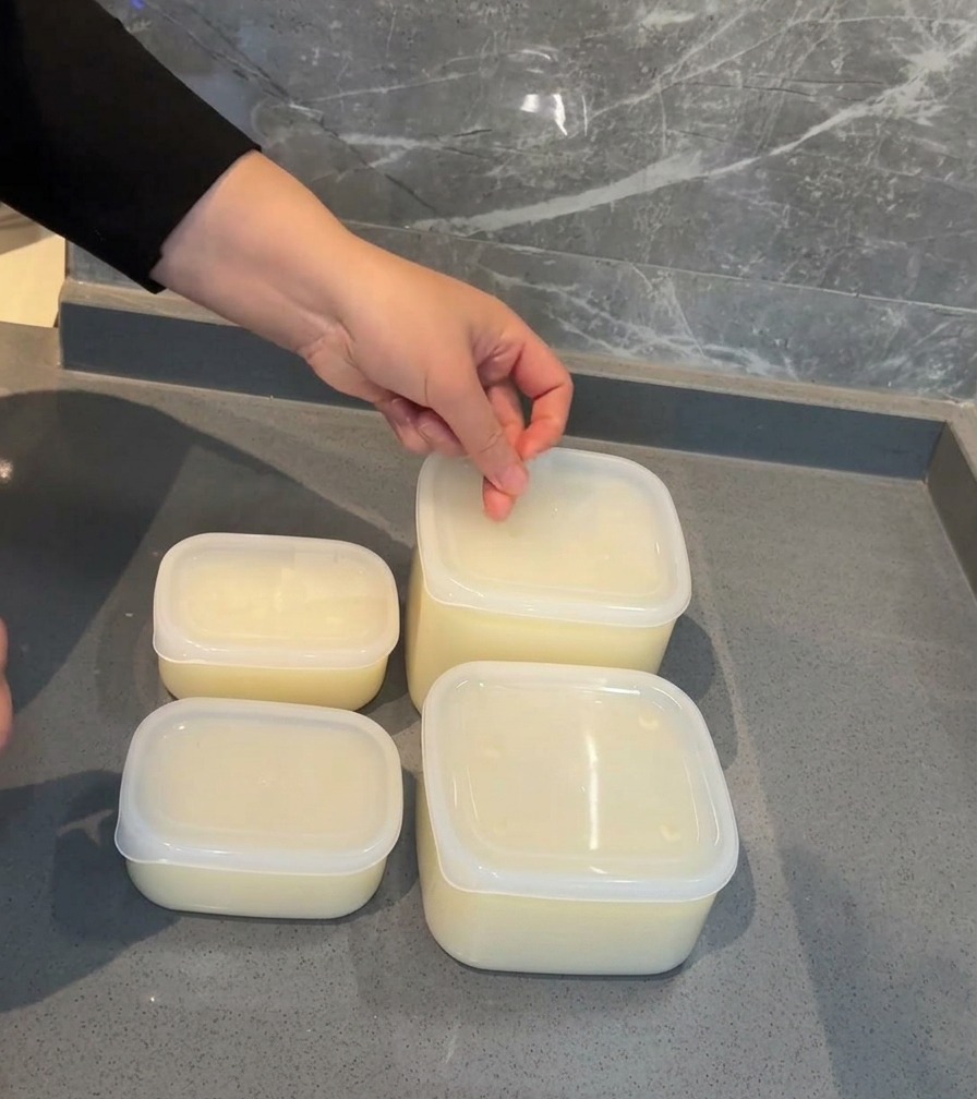 Eine Hand klebt ein weißes Datumsetikett auf den Deckel eines Plastikbehälters, der mit Schweinebrühe gefüllt ist.