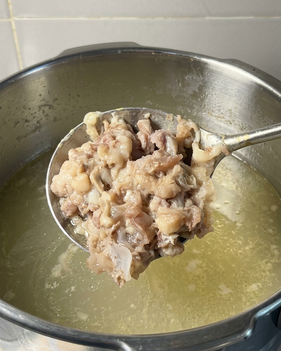 Eine Kelle voller dicker, zerstampfter Schweine- und Hühnerfleischmasse wird über einen Topf mit köchelnder Brühe gehalten.
