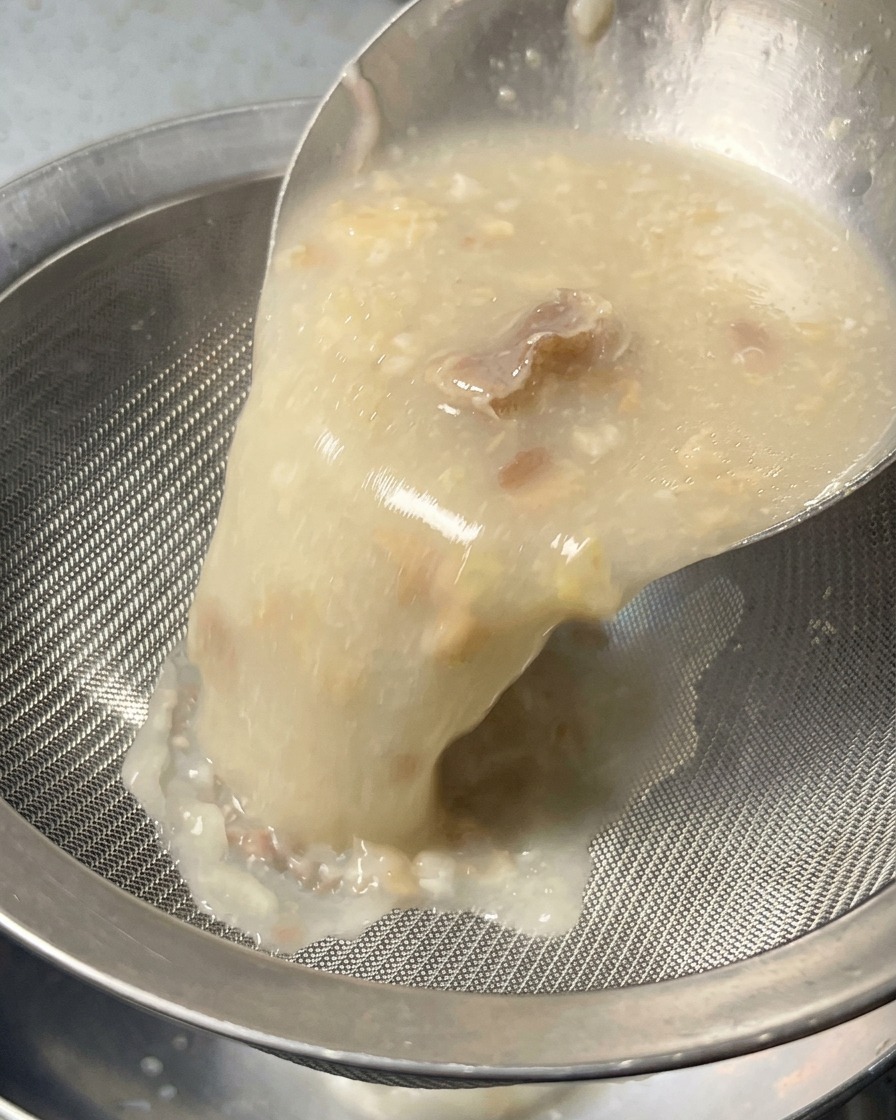 Eine dicke, opake weiße Brühe wird durch ein feines Sieb in eine Schüssel gegossen, um feste Stücke herauszufiltern.