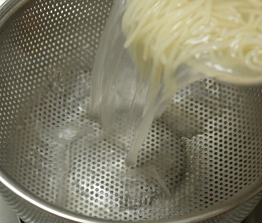 Ein Topf mit gekochten Ramen-Nudeln wird in ein Metallsieb gegossen, um das heiße Kochwasser abzutropfen.
