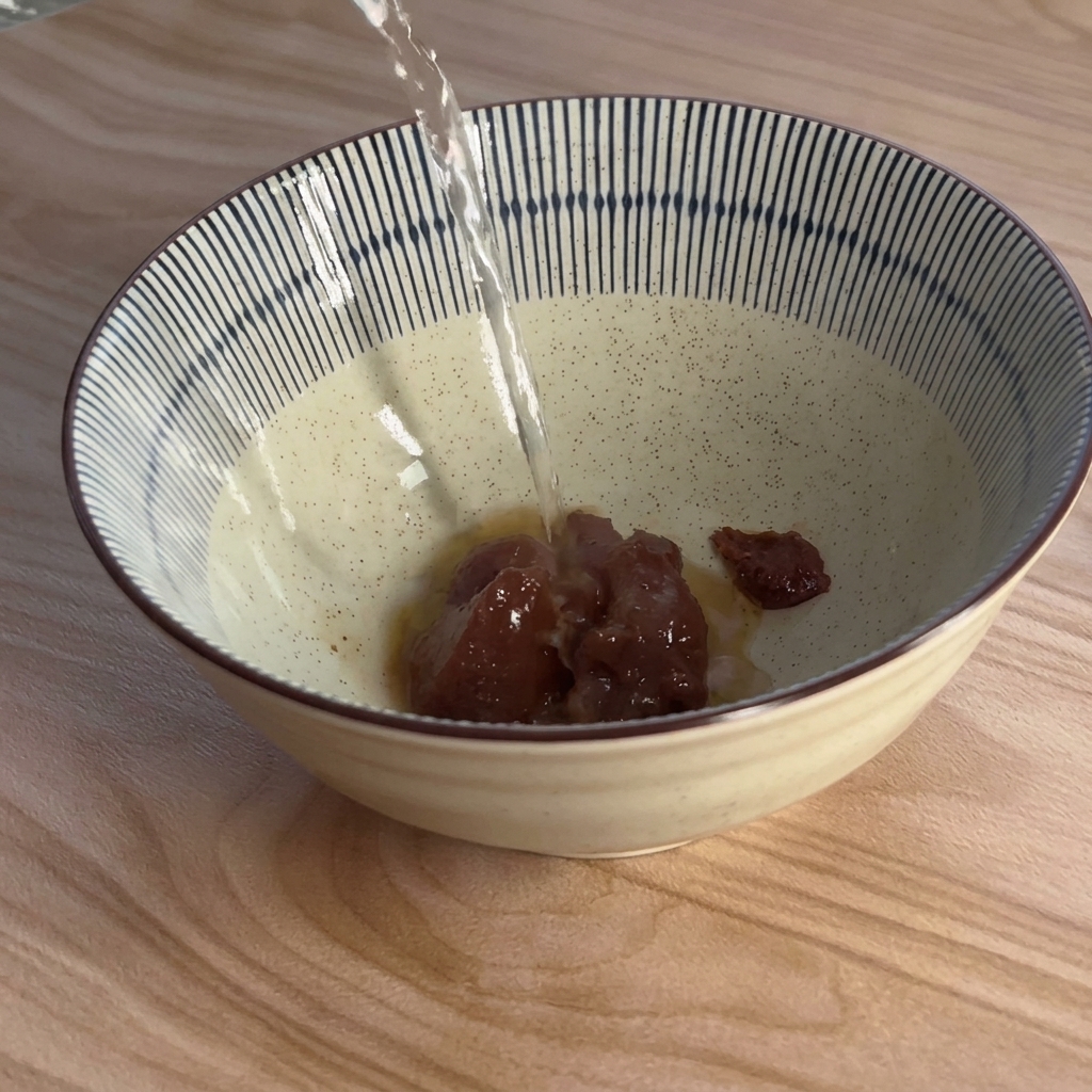 Heißes Wasser wird von oben in eine blau-weiß gestreifte Schüssel mit brauner Miso-Paste gegossen.