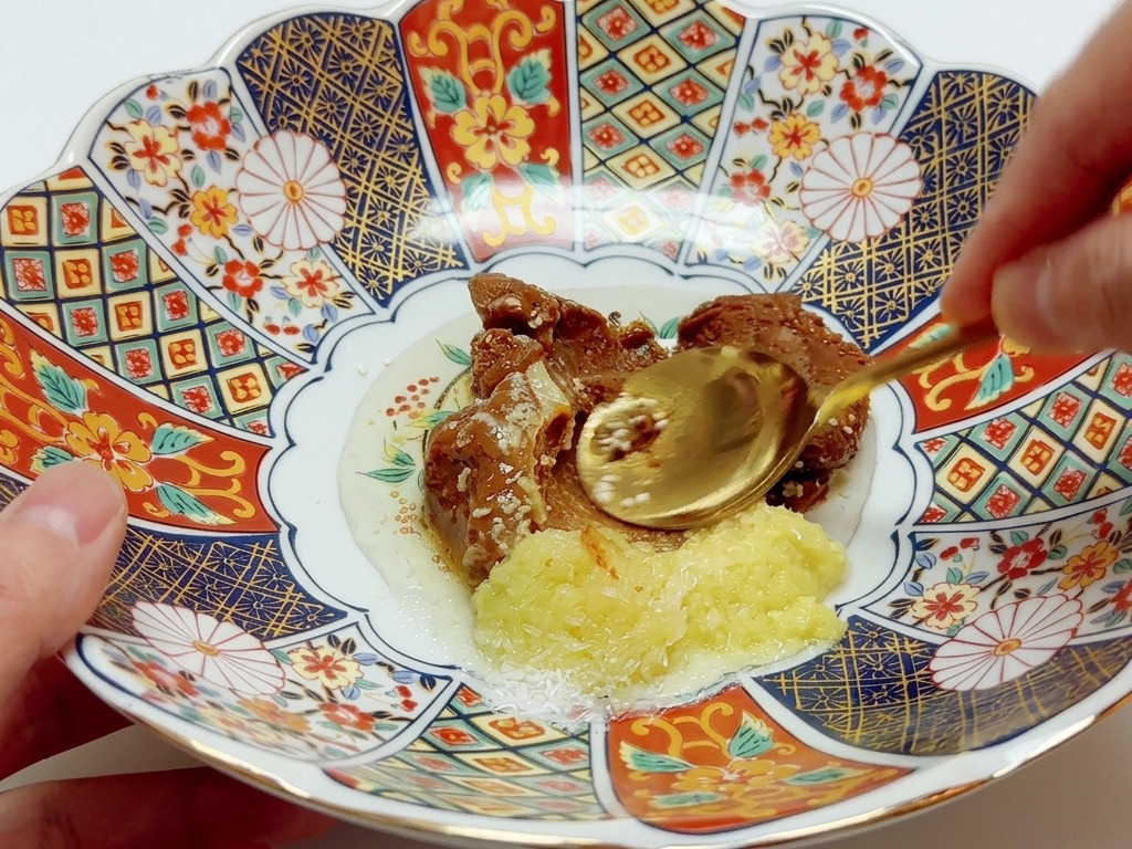 Ein Löffel vermengt verschiedene Pasten und Gewürze in einer bunten, verzierten Porzellanschüssel.