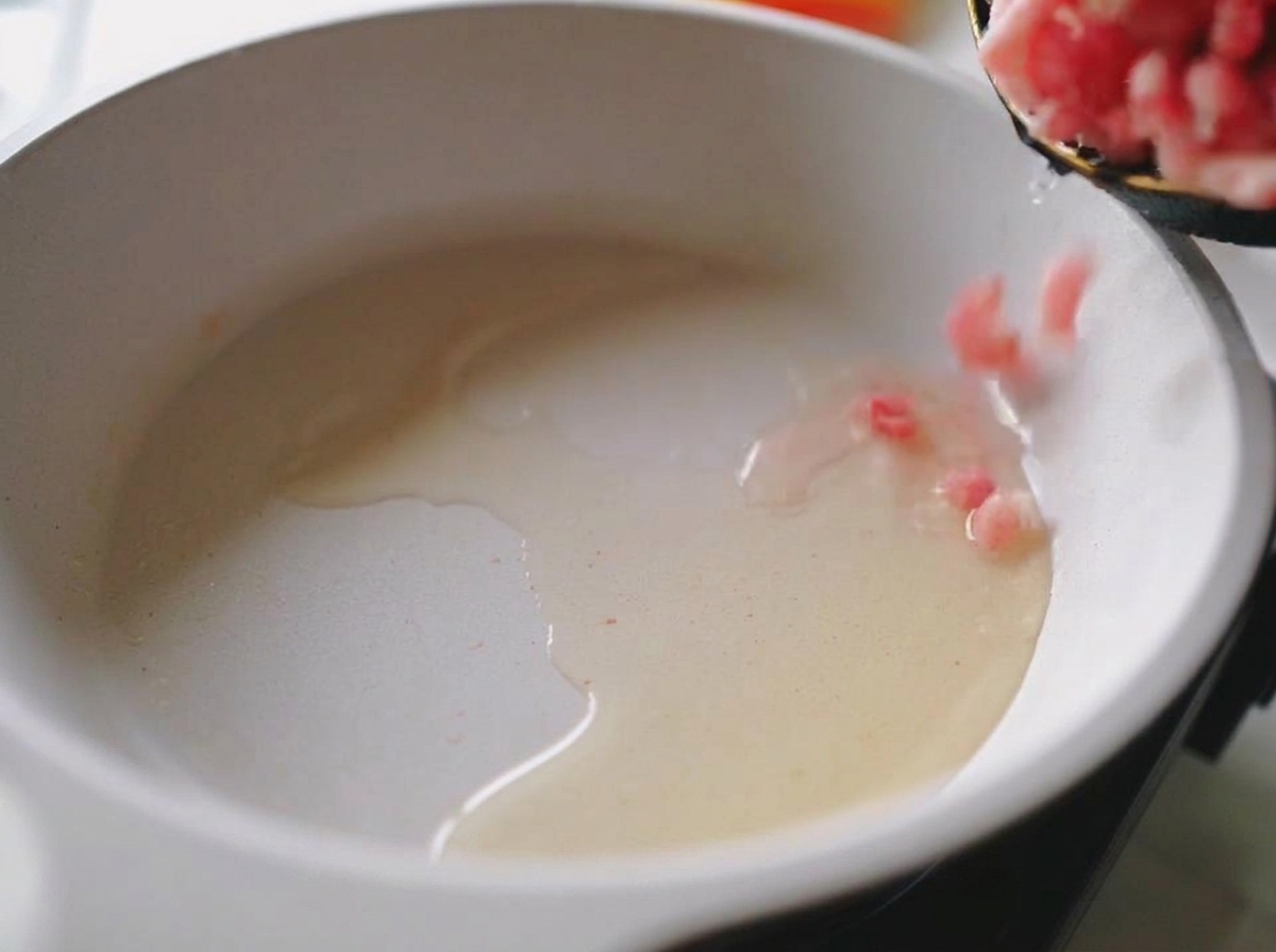 Frisches rosa Schweinehackfleisch wird in eine heiße Pfanne mit glänzendem Öl gegeben.