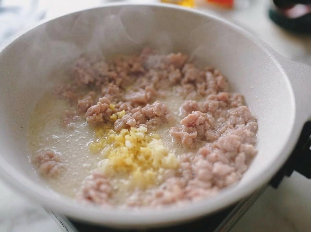 Gehackter Knoblauch und Ingwer werden unter das gebräunte Hackfleisch in der Pfanne gerührt.