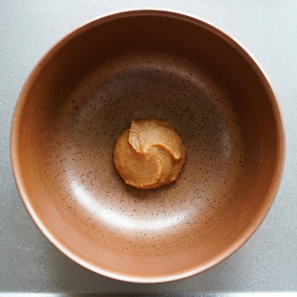 Ein Klecks dunkle Miso-Paste am Boden einer gesprenkelten Keramikschale.
