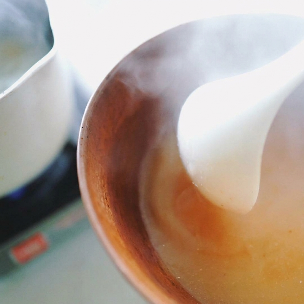 Eine weiße Schöpfkelle rührt heiße Flüssigkeit in eine Schale, um die Miso-Paste aufzulösen.