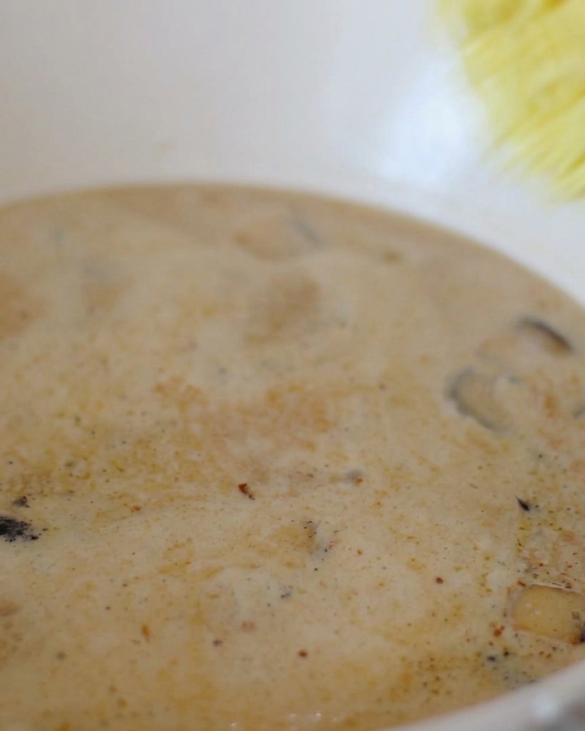 Ein Block gelbe Instant-Ramen-Nudeln wird in einen Topf mit brodelnder, cremiger weißer Brühe gegeben.