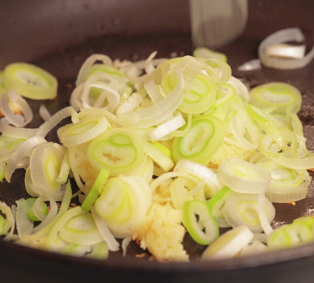 Rohes Schweinehackfleisch, gehackter Knoblauch und ein Haufen geschnittene Frühlingszwiebeln in einer dunklen Pfanne vor dem Kochen.