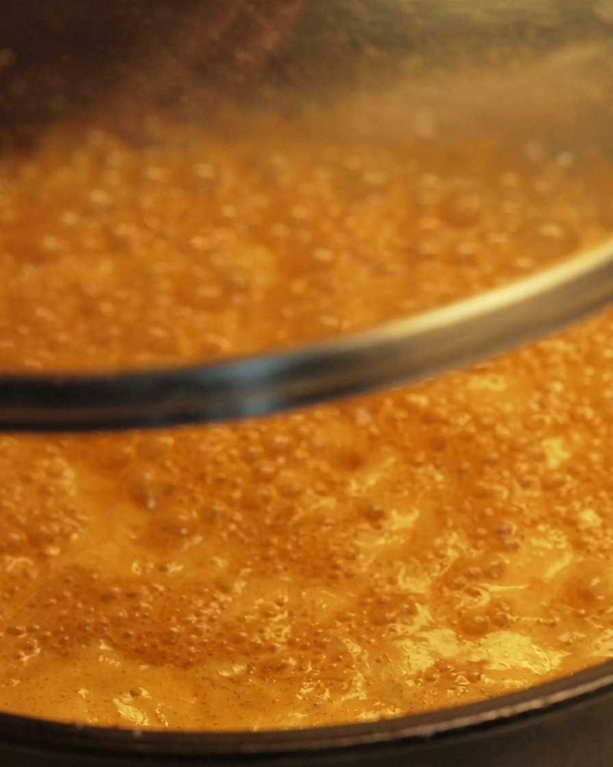 Ein klarer Glasdeckel wird auf eine Pfanne mit einer blubbernden, köchelnden orangefarbenen Sauce gesetzt.
