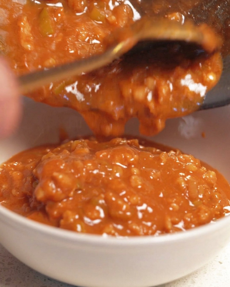 Reichhaltige, stückige, orangefarbene Dip-Sauce wird aus einer dunklen Pfanne in eine weiße Keramikschale gegossen.