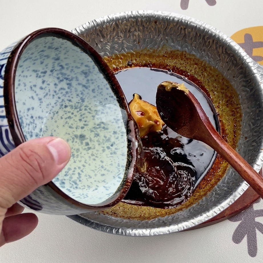 Klare Dashi-Brühe wird aus einer blau-weiß gemusterten Keramikschale in die dunkle Miso-Sauce gegossen.
